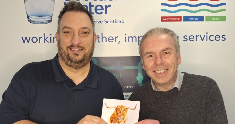 Clive Duncan, Communications Manager, and David Pascall, Project Manager, with Thank You Card from Customer Two individuals standing in front of a Scottish Water banner, one holding a Thank You card from a customer with an image of a highland cow on it.