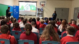 CWA employees stand in front of projector screen presenting to rows of pupils